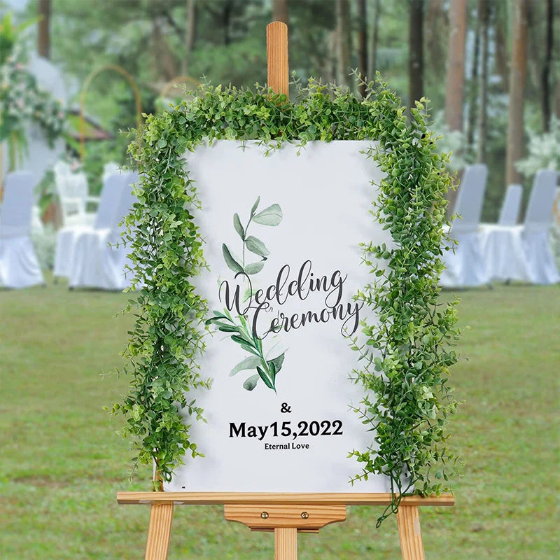 Guirlande d'eucalyptus artificielle encadrant un panneau indiquant 'Wedding Ceremony and May 15, 2022'