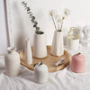 A collection of white ceramic vases and a plant arrangement on a light wooden tray.