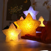 A hand holds a glowing yellow LED star light, illuminating a dark background with a faint moon and stars.