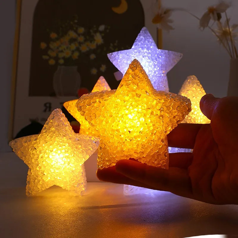 A hand holds a glowing yellow LED star light, illuminating a dark background with a faint moon and stars.