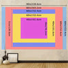 A colorful layered wall hanging design featuring pink, yellow, and blue geometric shapes on a light gray wall.