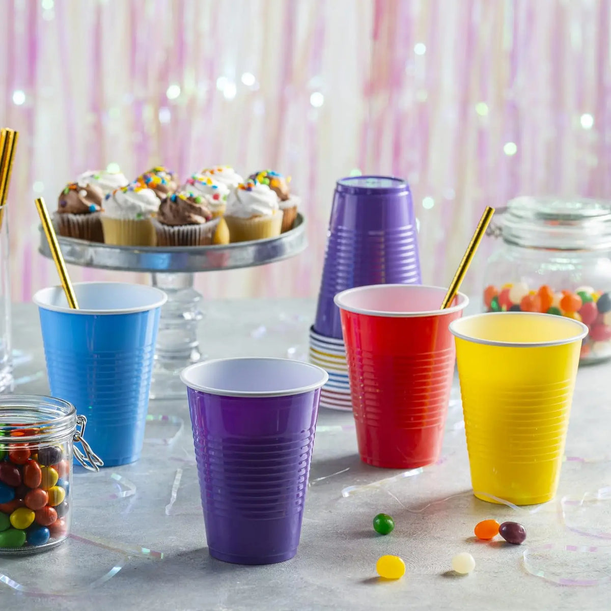 A collection of colorful disposable party cups in various shades of blue, purple, and red are displayed on a gray surface wit