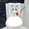 A white toilet decorated with a funny cartoon face and tongue, set against a tiled bathroom wall.