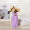 A purple plastic vase with an abstract folded design holds a bouquet of light pink and cream roses.