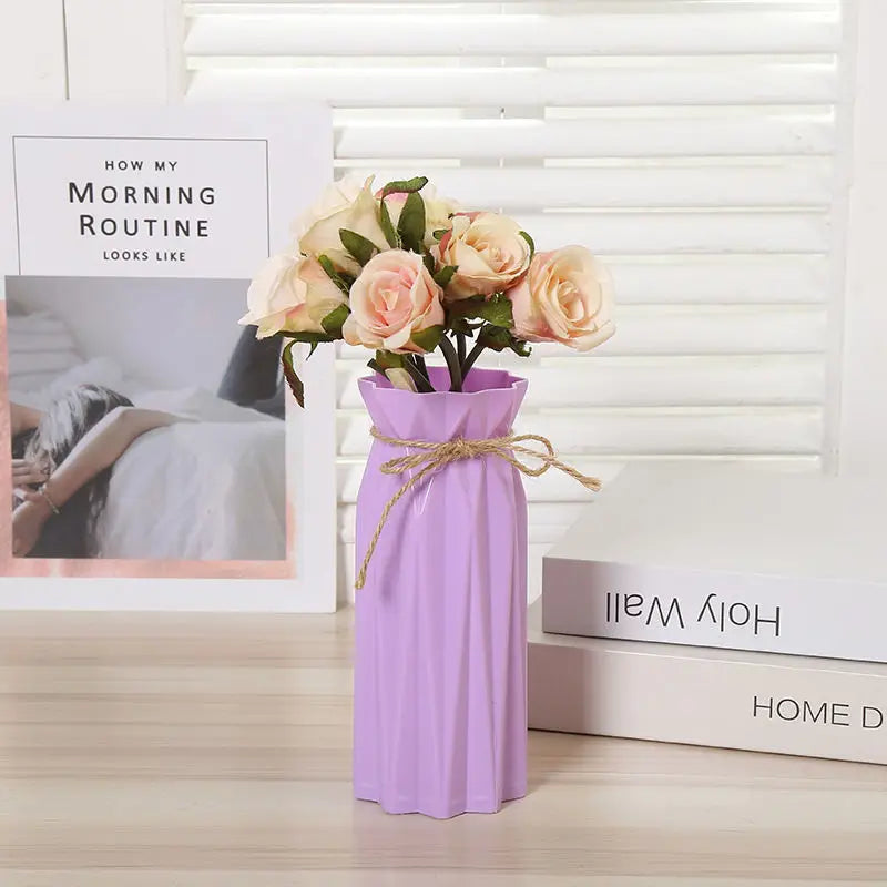 A purple plastic vase with an abstract folded design holds a bouquet of light pink and cream roses.