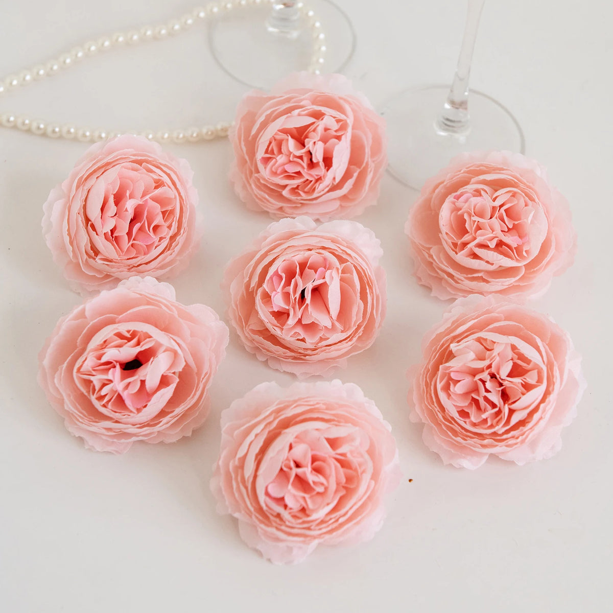A collection of pink silk peony artificial flowers arranged on a white surface.