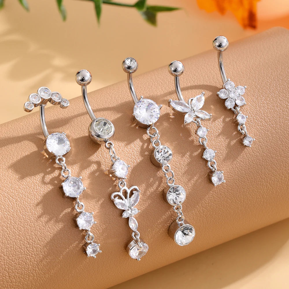 A set of five gold tone butterfly and flower belly rings displayed on a beige surface.