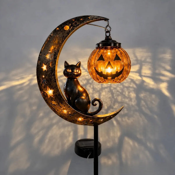 A decorative stake light featuring a crescent moon with stars and a black cat silhouette, illuminating a carved pumpkin.