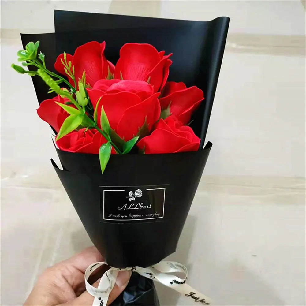 A bouquet of red roses in a black paper holder tied with a white ribbon.