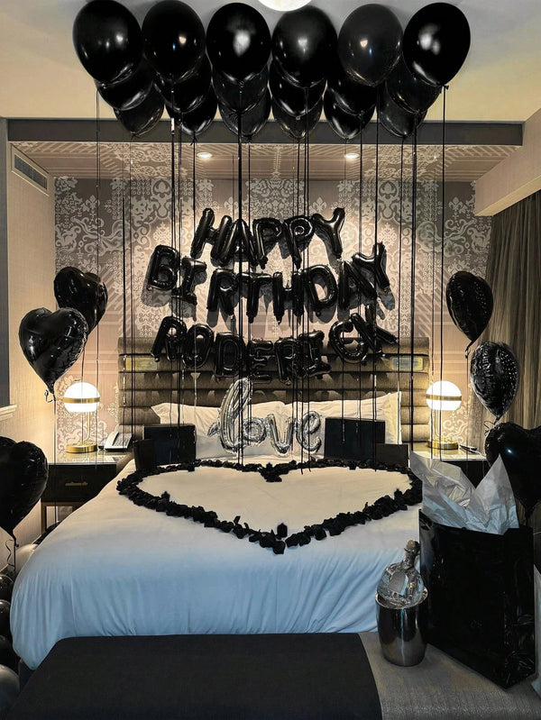 A bedroom decorated for a birthday party with black balloons and foil letters spelling 'HAPPY BIRTHDAY LOVE' above a bed.