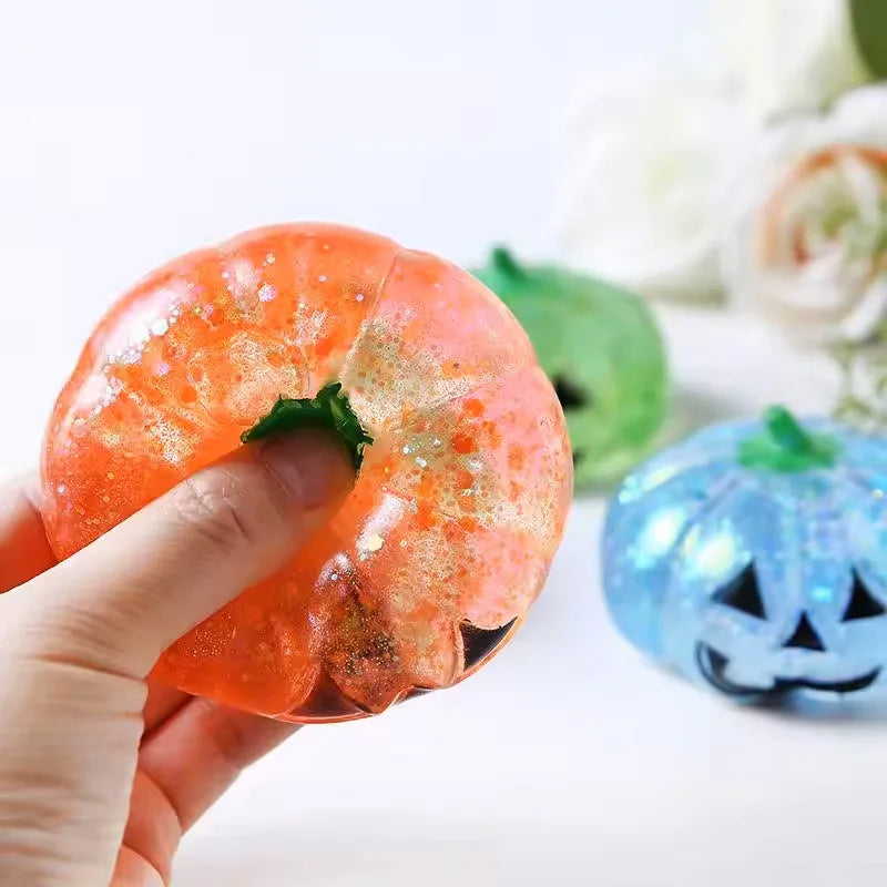 A hand holds an orange Halloween pumpkin stress ball with a slow rebound next to a green pumpkin.