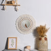 Miroir en macramé rond accroché au mur blanc à côté d'une étagère en bois et d'un vase de graminées séchées.