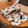 A beige canvas travel makeup bag with polka dots and a mirror is resting on a wooden table.