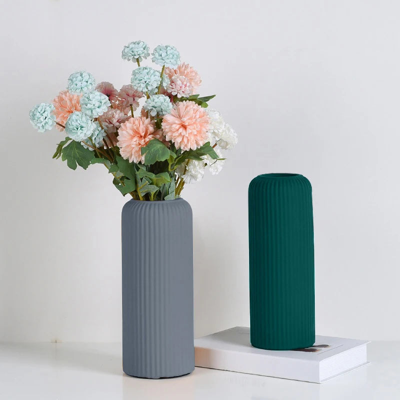 A bouquet of pink and blue flowers in a gray ribbed vase on a white surface.