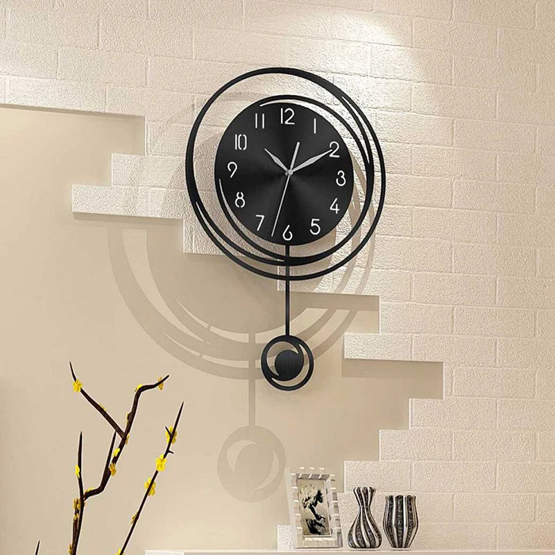 A modern black circular wall clock with Arabic numerals is mounted on a light-colored brick wall.