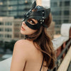 A woman wearing an elegant black fox masquerade mask with adjustable straps, looking over her shoulder.