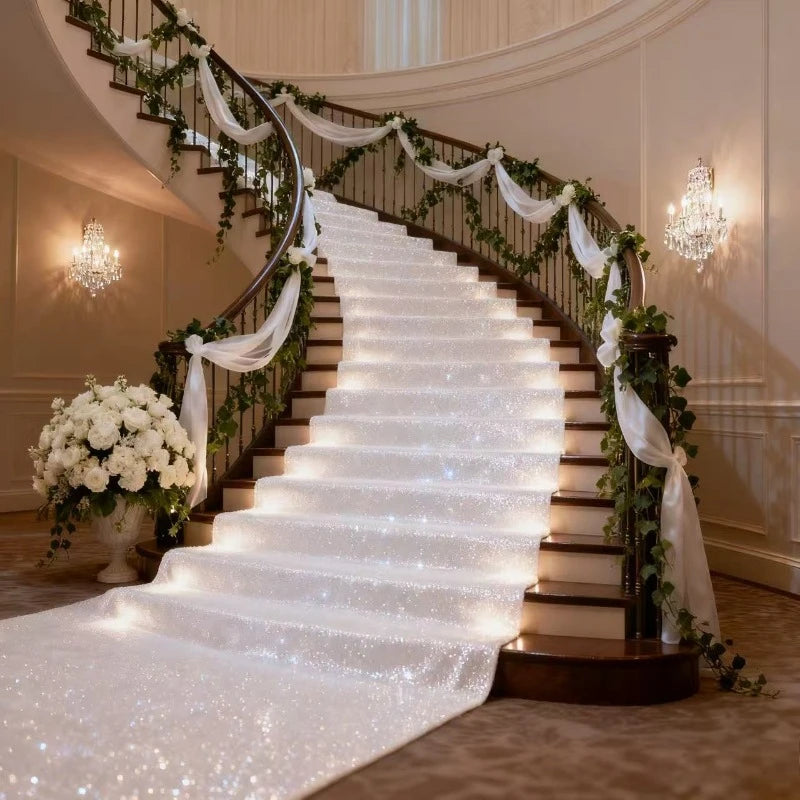 An elegant white sparkling aisle runner leading up a curved staircase decorated with greenery and white fabric.