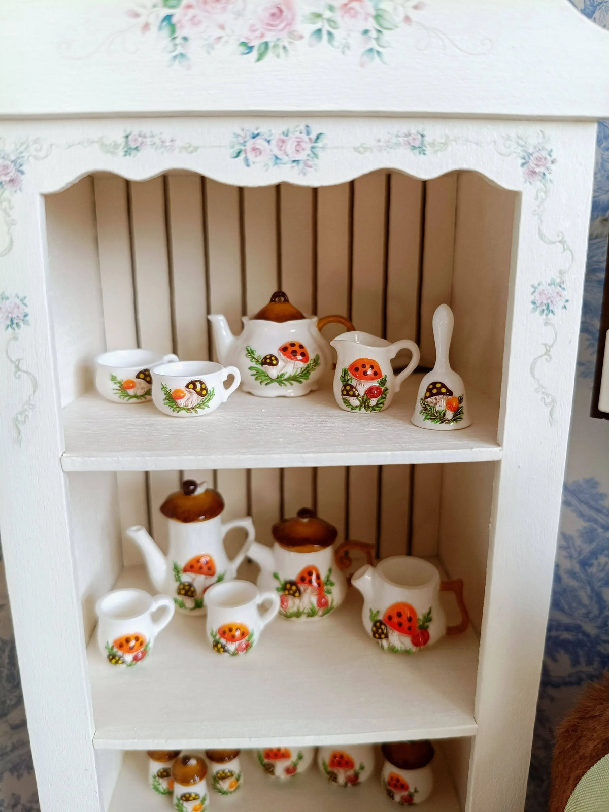 A collection of handcrafted miniature mushroom tableware for dollhouses displayed on a white shelf.