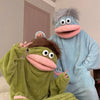 Two people in fuzzy monster onesies pajamas sitting on a bed
