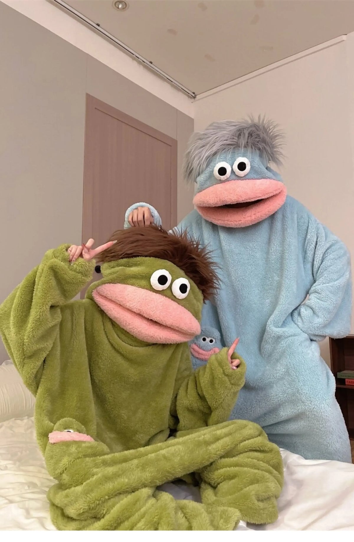 Two people in fuzzy monster onesies pajamas sitting on a bed