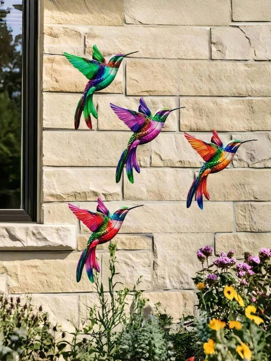 Four metal hummingbird wall decor figurines in vibrant colors mounted on a light-colored stone wall.
