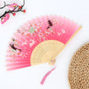 Pink folding fan with delicate floral patterns and a bamboo texture in the background