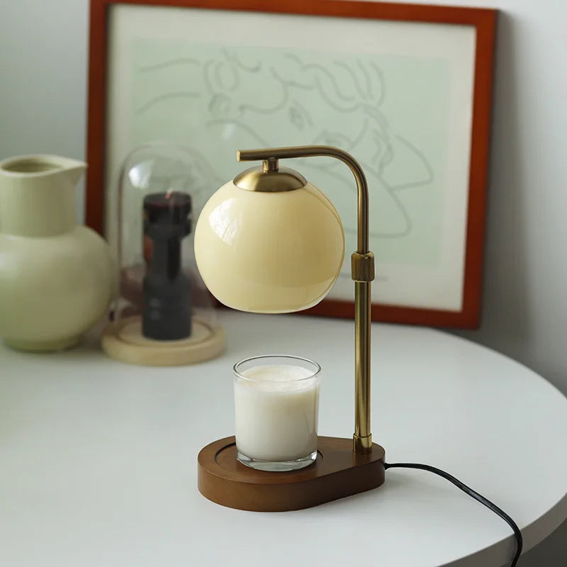 A brass aromatherapy wax melting lamp with a glass bulb sits on a wooden base next to a framed drawing.