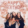 Three women in black dresses wear crowns and hold red drinks in front of a rose gold balloon garland.