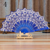 A blue lace folding hand fan with white embroidery displayed on a wooden stand.
