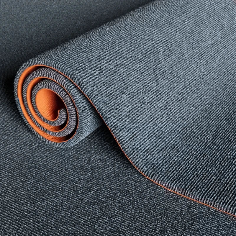 Roll of dark gray artificial grass carpet with an orange accent, showing the texture and coil.