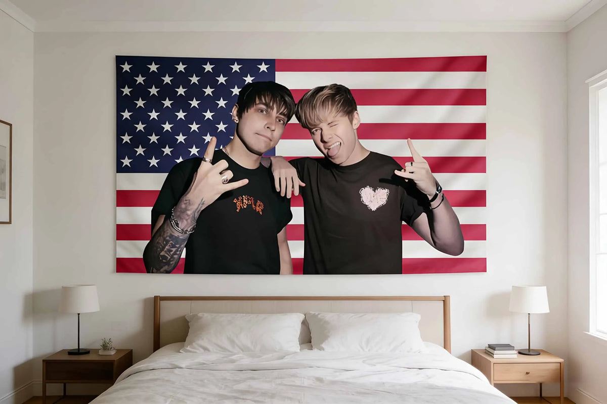 Two young men pose in front of an American flag tapestry hanging above a bed.