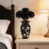 A black gothic skull resin decorative vase filled with dark flowers sits on a bedside table next to a lamp.