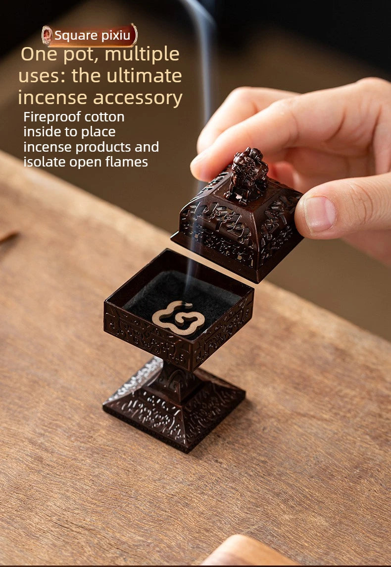 A hand holds a square incense accessory made of dark wood, designed to safely hold and isolate open incense flames.