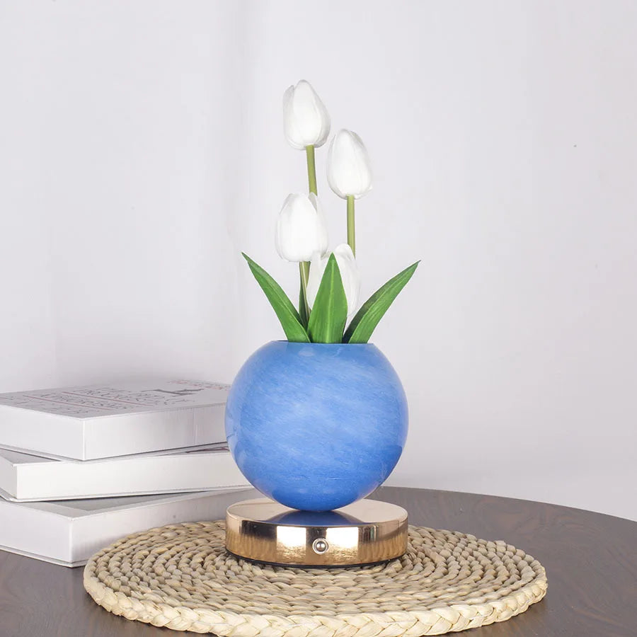 A vase of white tulips in a blue ceramic pot on a woven mat.