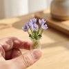 A hand holds a clear glass vase filled with purple lavender flowers.