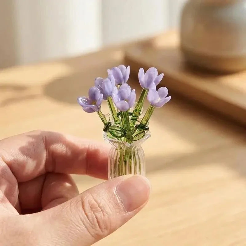 A hand holds a clear glass vase filled with purple lavender flowers.