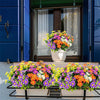A vibrant bouquet of silk daisies in various colors is displayed on a black metal rack.