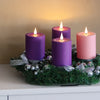 A display of purple and pink flameless LED candles arranged on a green wreath on a white table.