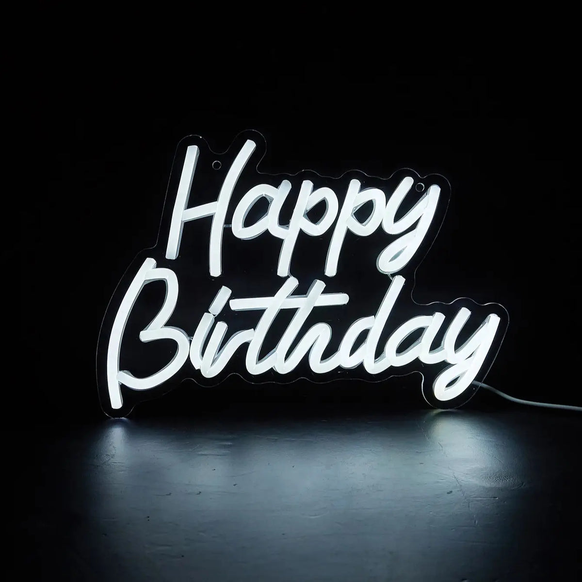 A glowing white LED neon sign spelling out Happy Birthday against a dark background.