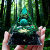 Hand holding a clear resin pyramid with green inclusions and a copper coil against a dark background.
