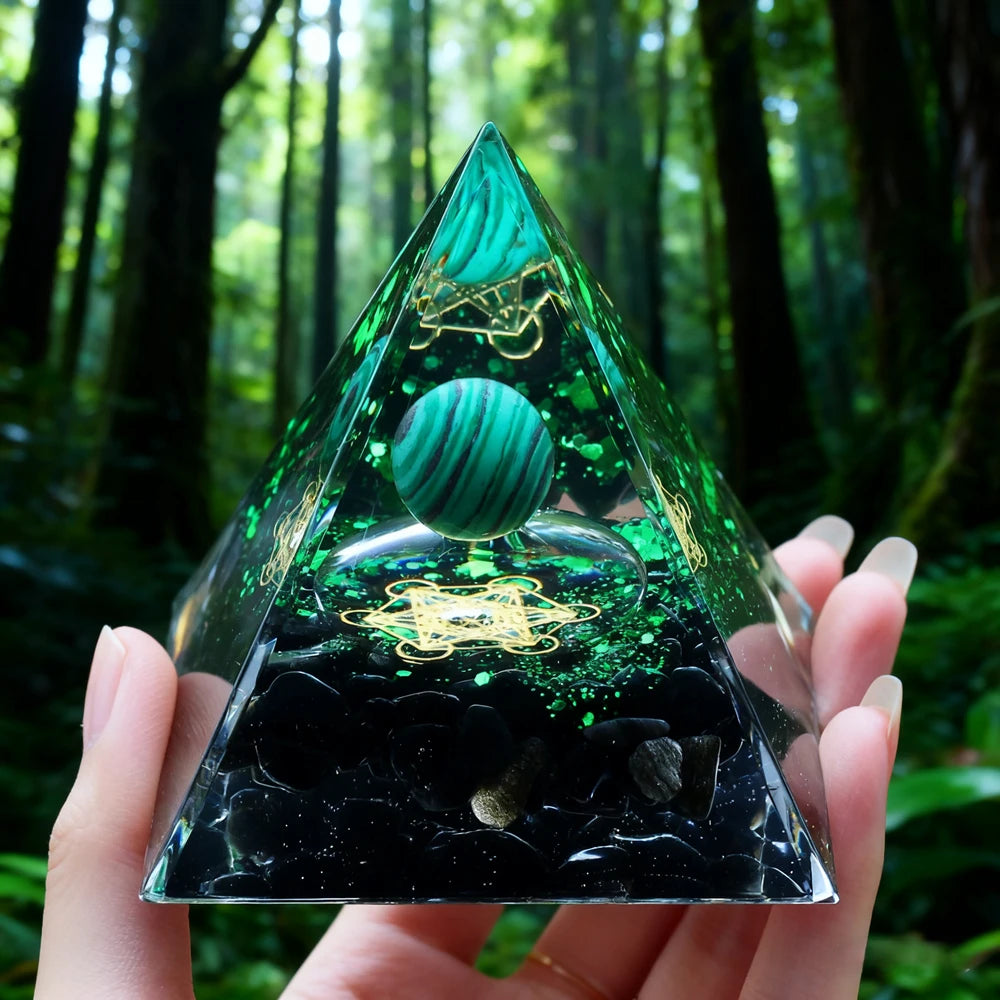 Hand holding a clear resin pyramid with green inclusions and a copper coil against a dark background.