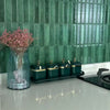 Green ceramic jars lined up on a black tray against a teal tiled backsplash.