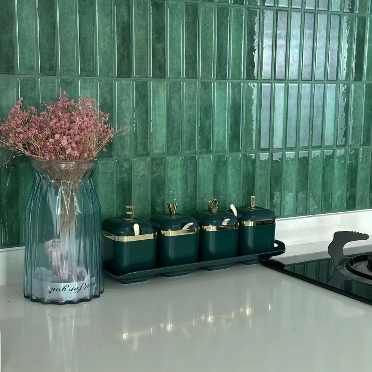 Green ceramic jars lined up on a black tray against a teal tiled backsplash.