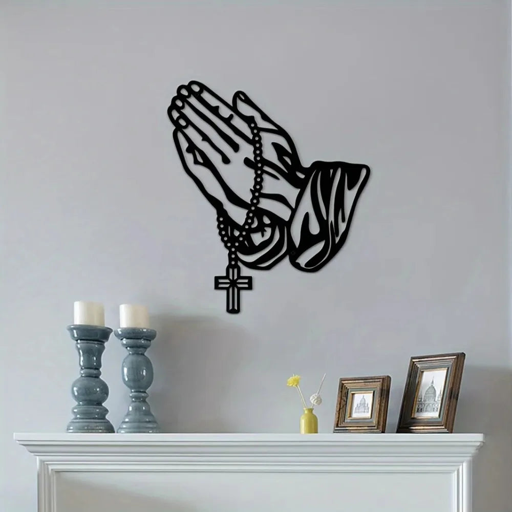 Black silhouette of praying hands with a cross pendant wall art on a white mantelpiece