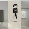 A black cartoon cat wall clock with a white bow and swinging tail mounted on a light gray wall.
