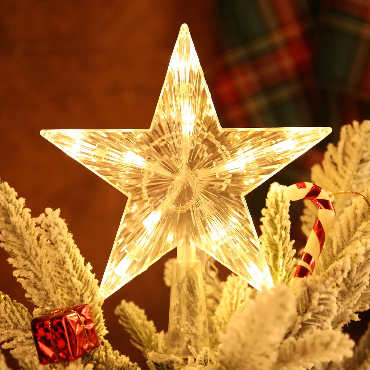 An LED glowing star topper decorated with white fluffy branches and a candy cane on a Christmas tree.