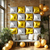 A display of silver and gold foil balloon wall panels arranged in a grid, set against a brick wall with greenery.