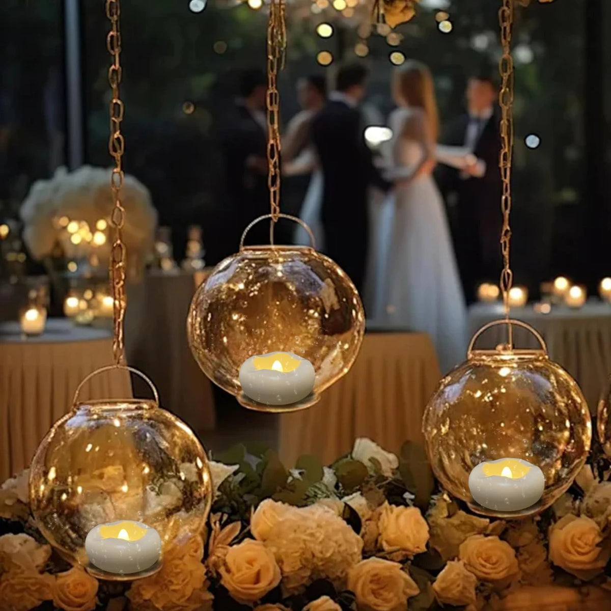 A close-up of a gold-toned hanging lantern with a white candle, set amidst floral arrangements.