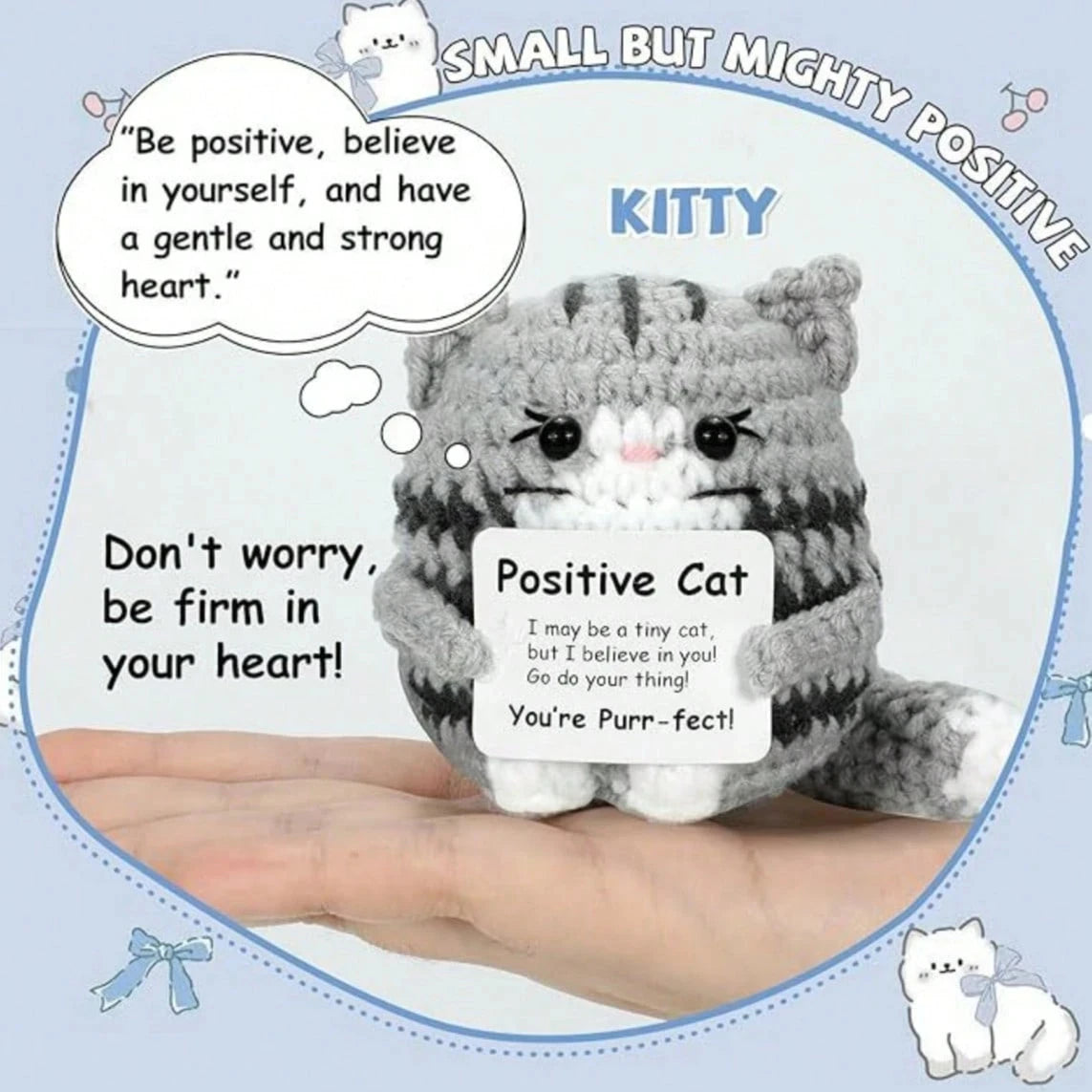 A handmade crochet mini cat plush toy with gray and white stripes is shown resting on a person's hand.