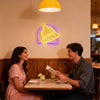 A woman and a man sit at a wooden table in a restaurant with a neon bell sign hanging on the wall.